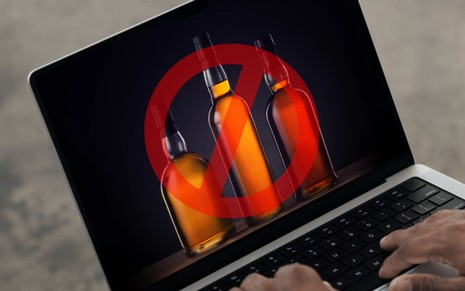 Notebook com a tela aberta mostrando garrafas de uísque, marcadas com o símbolo de proibido