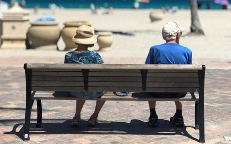 Idosos sentados em banco na praia