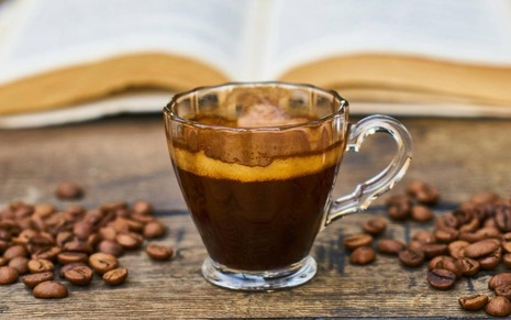 Imagem de café preto e grãos de café espalhados em mesa