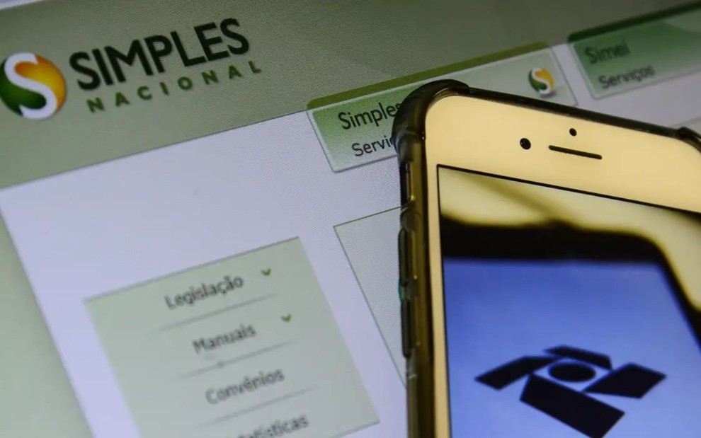 Celular com tela da Receita Federal e, ao fundo, página do site do Simples Nacional.
