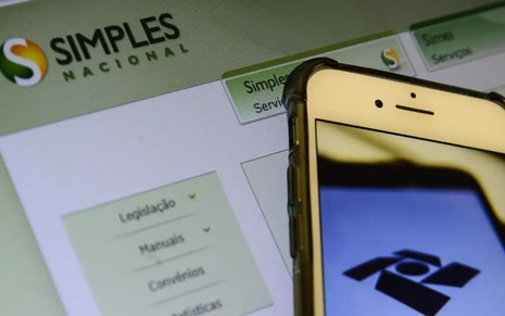 Celular com tela da Receita Federal e, ao fundo, página do site do Simples Nacional.