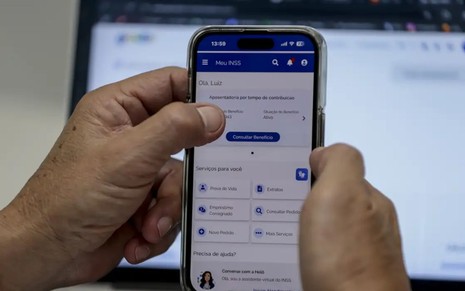 Mãos segurando um celular no site Meu INSS