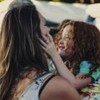 Mãe carrega seu filho no colo em praia