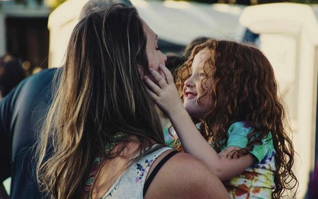 Mãe carrega seu filho no colo em praia