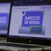 Notebook com a tela escrita "Imposto de Renda 2025" e um celular posicionado à frente.
