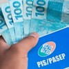 Homem segura notas de 100 reais e um documento escrito PIS/Pasep
