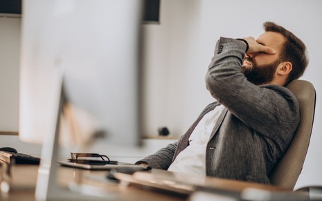 Homem triste com a mão no rosto, sentado no escritório, aparentando frustração profissional.