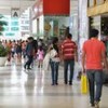 Pessoas caminham pelos corredores do shopping, carregando sacolas de compras nas mãos.
